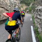 Cyclists on a mountain road with rocky cliffs and greenery.